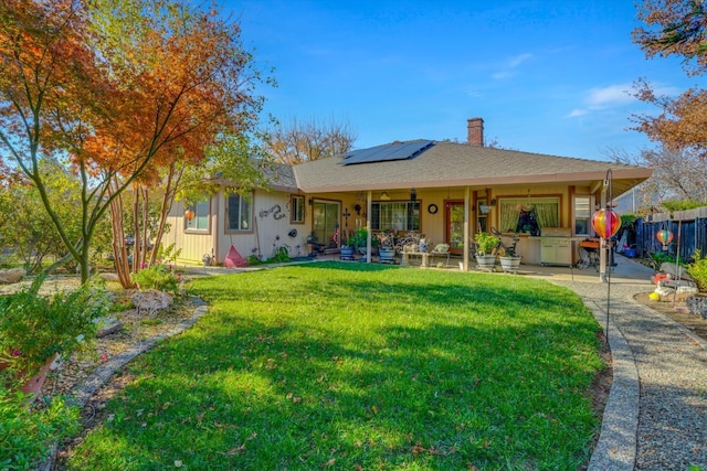 ranch-style home featuring solar panels, fence, roof with shingles, a chimney, and a front yard