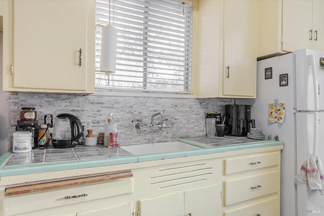 kitchen featuring backsplash, tile countertops, cream cabinets, and sink