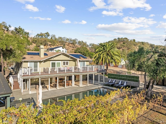 back of property with a patio area, a balcony, a pool, and solar panels