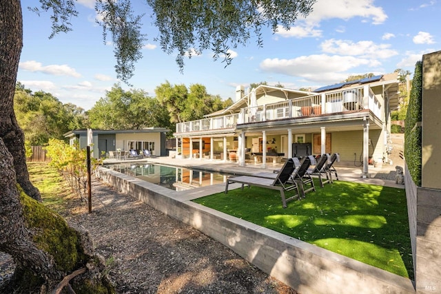 rear view of property featuring a lawn, a balcony, a patio, and solar panels