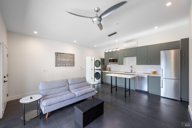 living room with an AC wall unit, ceiling fan, stacked washer / drying machine, and sink