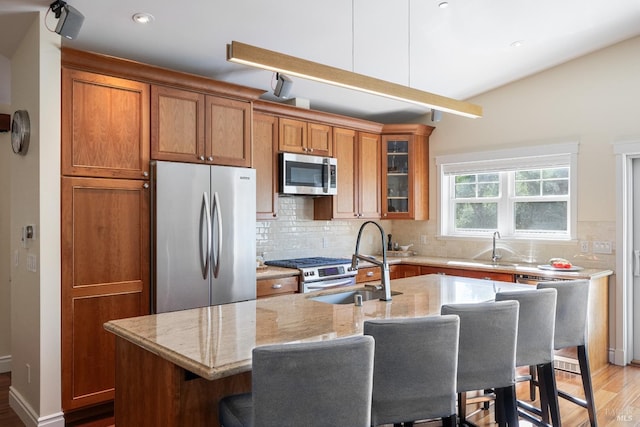 kitchen featuring appliances with stainless steel finishes, light wood-type flooring, backsplash, light stone counters, and a kitchen island with sink