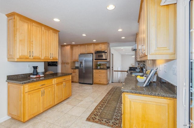 kitchen with appliances with stainless steel finishes, light tile patterned floors, dark stone countertops, and sink