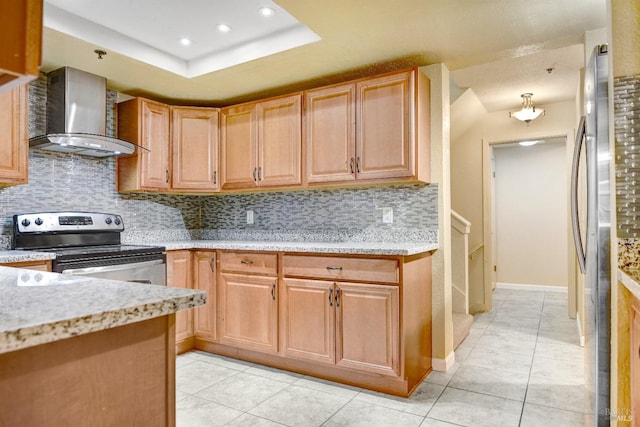 kitchen with a raised ceiling, wall chimney exhaust hood, light tile patterned floors, appliances with stainless steel finishes, and tasteful backsplash