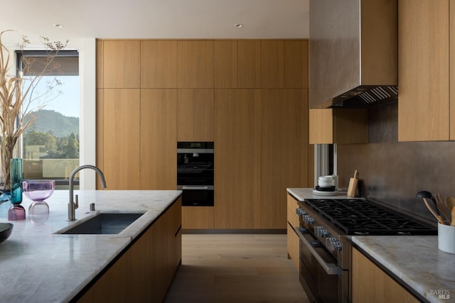 kitchen with double oven range, light stone counters, modern cabinets, wall chimney exhaust hood, and a sink