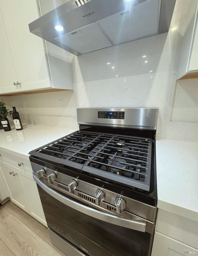 details featuring stainless steel range with gas cooktop, white cabinets, light hardwood / wood-style floors, and ventilation hood