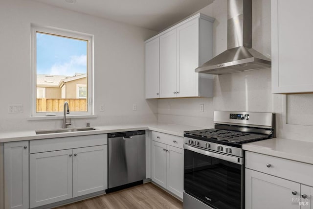 kitchen featuring stainless steel appliances, white cabinetry, wall chimney exhaust hood, and sink