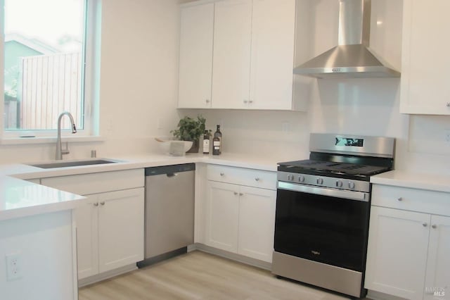 kitchen with appliances with stainless steel finishes, light wood-type flooring, wall chimney exhaust hood, sink, and white cabinetry