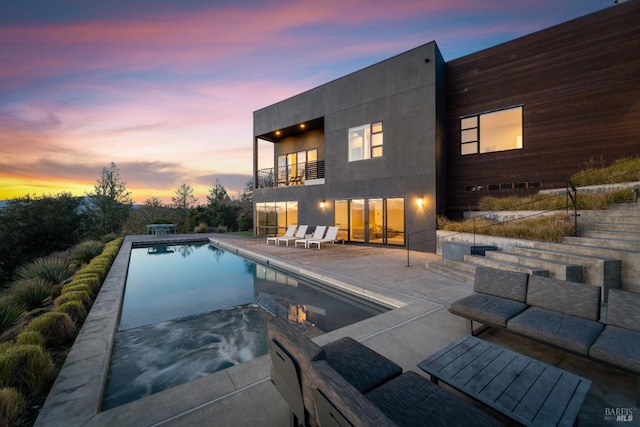 pool at dusk featuring an in ground hot tub, an outdoor living space, and a patio