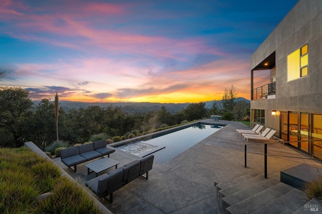 pool at dusk featuring an outdoor living space and a patio