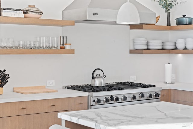 kitchen with light stone counters, gas stove, hanging light fixtures, and exhaust hood