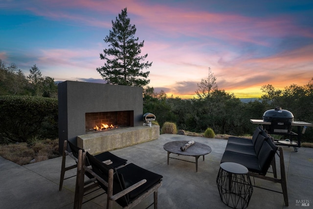 patio terrace at dusk featuring an outdoor fireplace and a grill