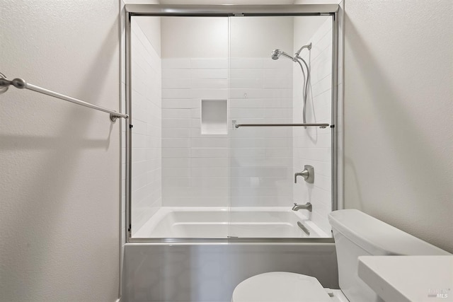 full bathroom with toilet, enclosed tub / shower combo, and a textured wall