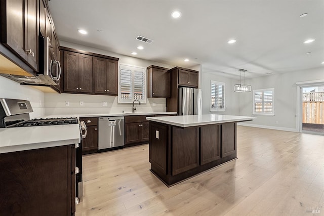 kitchen with dark brown cabinetry, light wood finished floors, appliances with stainless steel finishes, light countertops, and a sink