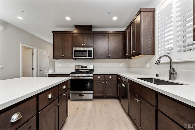 kitchen with dark brown cabinetry, a sink, light countertops, appliances with stainless steel finishes, and light wood finished floors