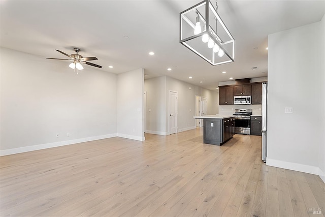 kitchen featuring stainless steel appliances, a kitchen island, open floor plan, light countertops, and light wood-type flooring