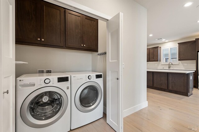 laundry room featuring a sink, separate washer and dryer, light wood-style flooring, and cabinet space