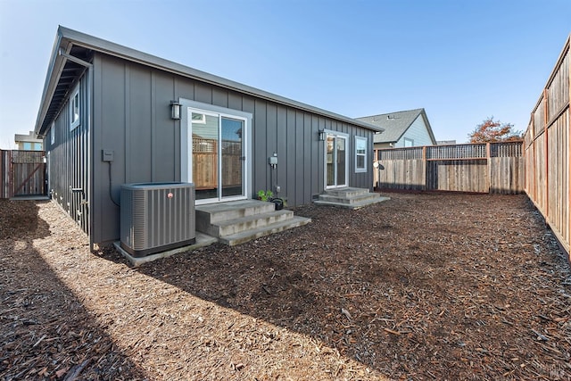 rear view of property with entry steps, central air condition unit, board and batten siding, and a fenced backyard