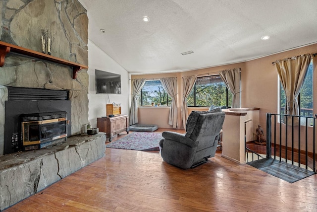 living room featuring a textured ceiling, hardwood / wood-style flooring, a stone fireplace, and lofted ceiling