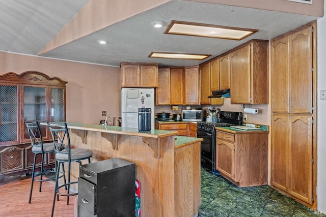 kitchen with a textured ceiling, a breakfast bar, black gas range oven, and white refrigerator