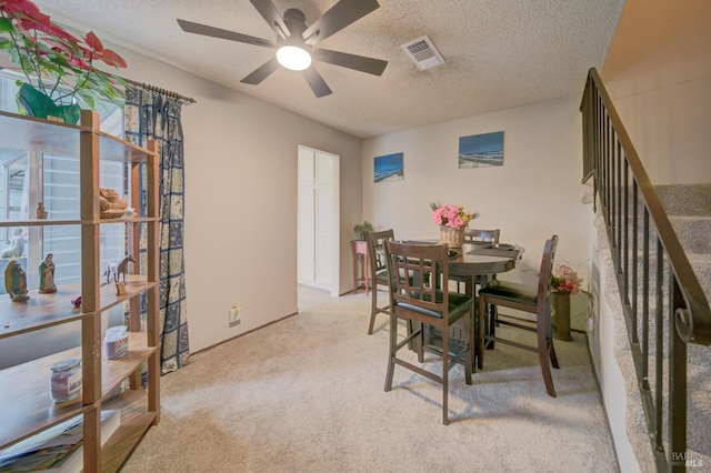 dining space with a textured ceiling, ceiling fan, and light carpet