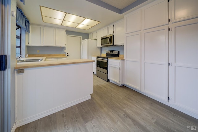 kitchen with kitchen peninsula, appliances with stainless steel finishes, sink, light hardwood / wood-style floors, and white cabinetry