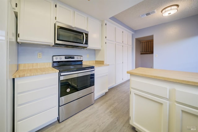 kitchen featuring light wood-type flooring, appliances with stainless steel finishes, a textured ceiling, and white cabinetry