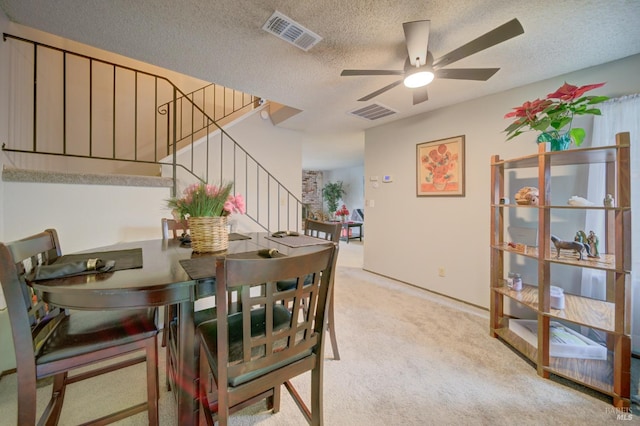 dining space featuring a textured ceiling, light colored carpet, and ceiling fan