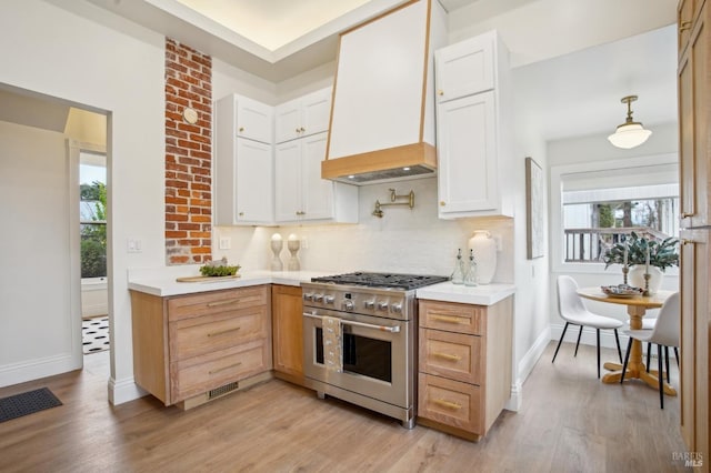 kitchen featuring premium range hood, pendant lighting, tasteful backsplash, white cabinets, and gas range