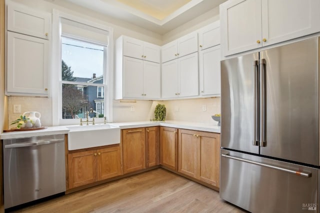 kitchen with appliances with stainless steel finishes, tasteful backsplash, sink, white cabinets, and light wood-type flooring