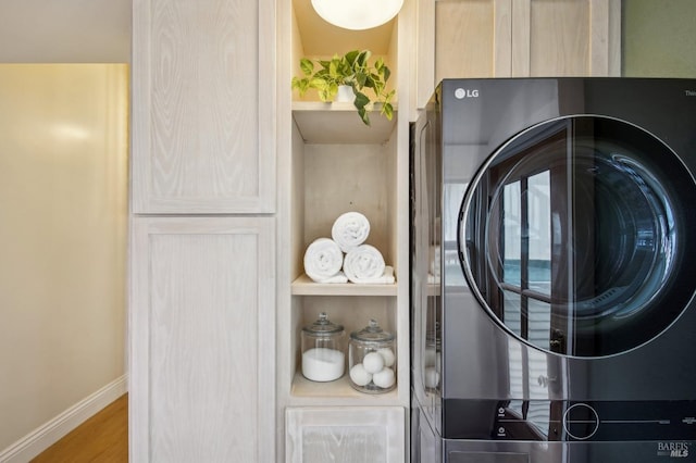 clothes washing area with hardwood / wood-style flooring, cabinets, and stacked washing maching and dryer