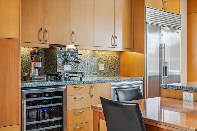 kitchen featuring stainless steel built in refrigerator, backsplash, stone countertops, and wine cooler