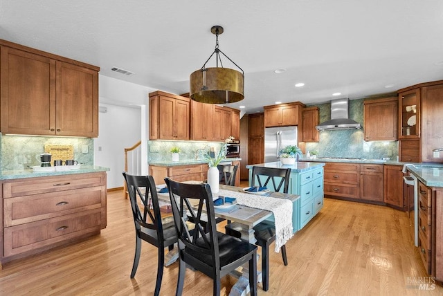 kitchen featuring pendant lighting, wall chimney range hood, tasteful backsplash, light hardwood / wood-style floors, and stainless steel appliances