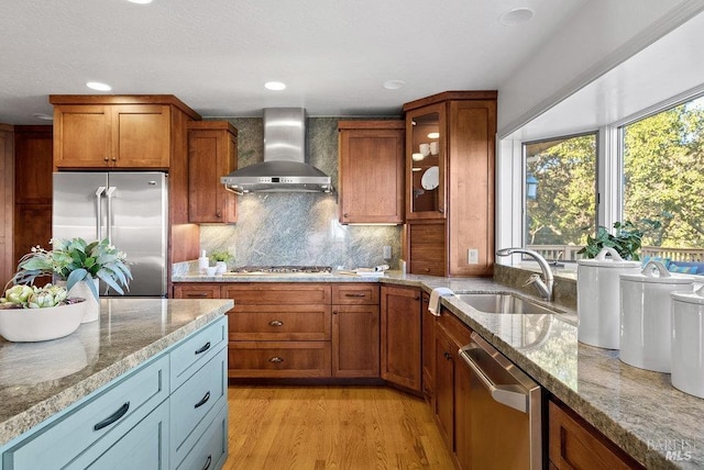 kitchen featuring sink, light hardwood / wood-style flooring, wall chimney exhaust hood, light stone countertops, and stainless steel appliances