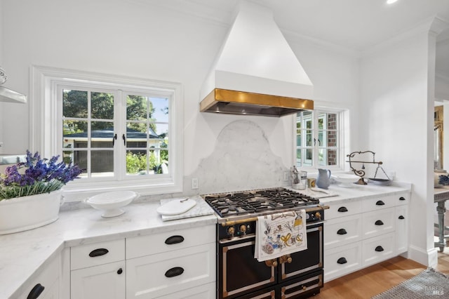 kitchen featuring light stone counters, custom range hood, white cabinets, and high end stainless steel range oven