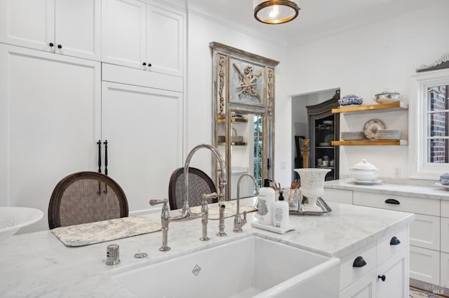 kitchen featuring light stone countertops, white cabinetry, ornamental molding, and sink