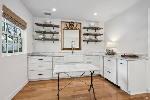 kitchen with white cabinets, light hardwood / wood-style floors, light stone countertops, and sink