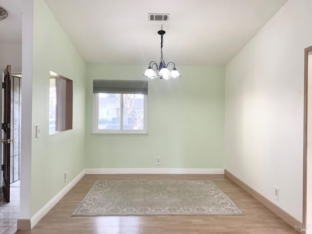 spare room with a chandelier, light wood-type flooring, visible vents, and baseboards