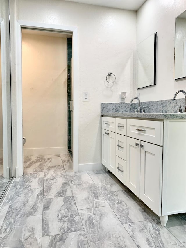 full bathroom with marble finish floor, double vanity, a shower stall, and baseboards