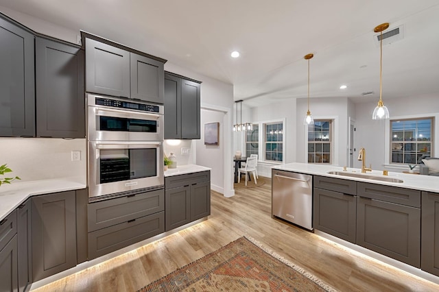 kitchen featuring light wood-type flooring, appliances with stainless steel finishes, sink, and pendant lighting