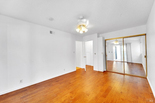 unfurnished bedroom with wood-type flooring, a textured ceiling, a closet, and ceiling fan