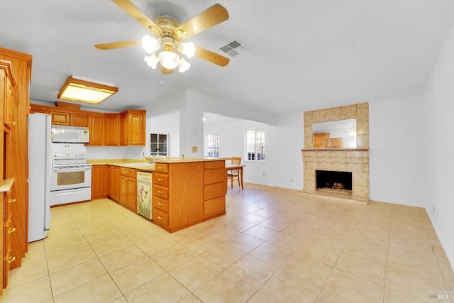 kitchen with kitchen peninsula, white appliances, ceiling fan, a fireplace, and light tile patterned flooring