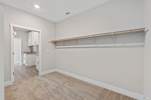 walk in closet with light colored carpet and sink