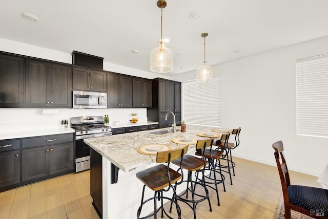 kitchen featuring sink, hanging light fixtures, stainless steel appliances, a kitchen island with sink, and light wood-type flooring