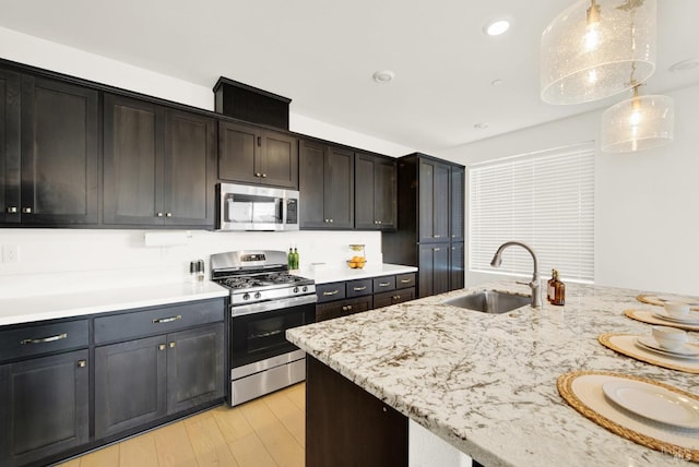 kitchen featuring sink, hanging light fixtures, stainless steel appliances, light stone counters, and light hardwood / wood-style floors