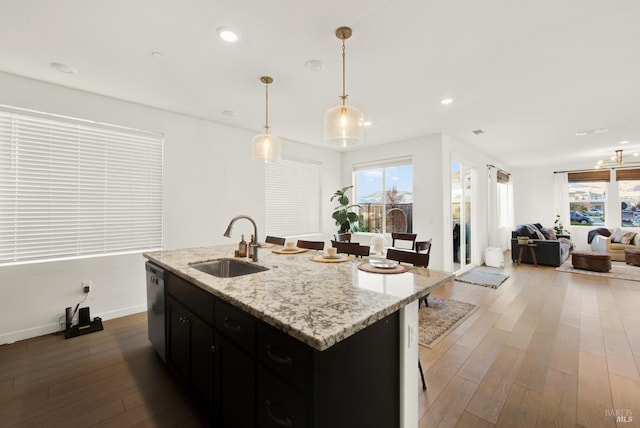 kitchen with stainless steel dishwasher, sink, pendant lighting, a center island with sink, and hardwood / wood-style floors