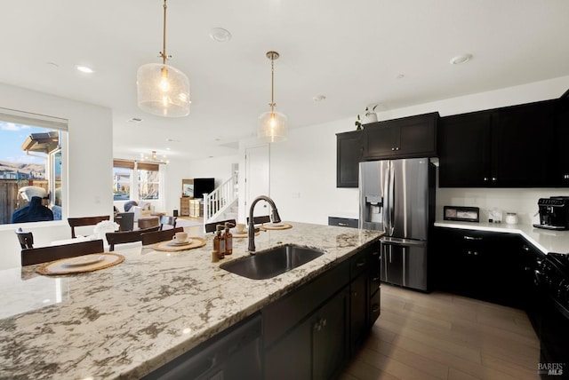 kitchen with light stone countertops, appliances with stainless steel finishes, sink, light hardwood / wood-style flooring, and hanging light fixtures