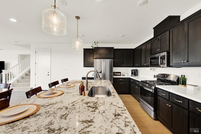 kitchen with a kitchen bar, appliances with stainless steel finishes, light wood-type flooring, sink, and hanging light fixtures