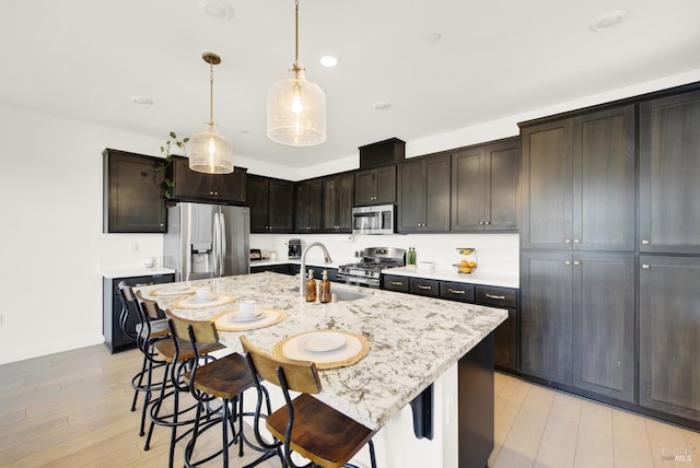 kitchen with pendant lighting, stainless steel appliances, light hardwood / wood-style floors, and an island with sink