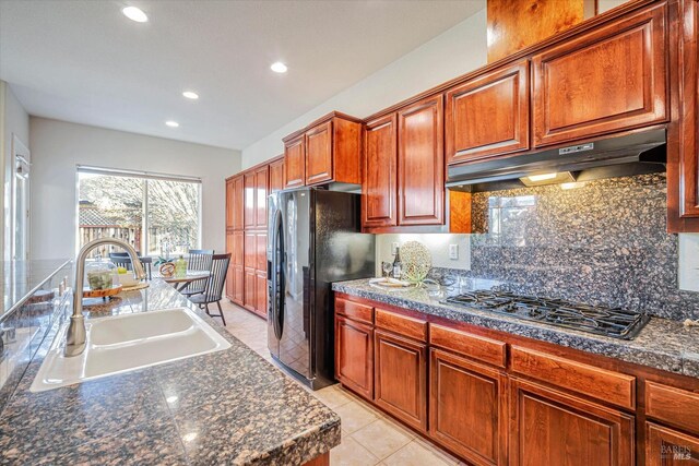 kitchen with backsplash, black fridge, stainless steel gas cooktop, light tile patterned flooring, and sink